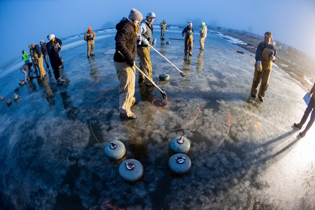 fish-eye lens used to capture scene on ice with people and their curling stones and brooms