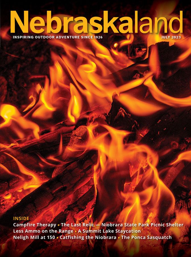 July 2023 Nebraskaland Magazine cover featuring logs on fire in a fire pit.