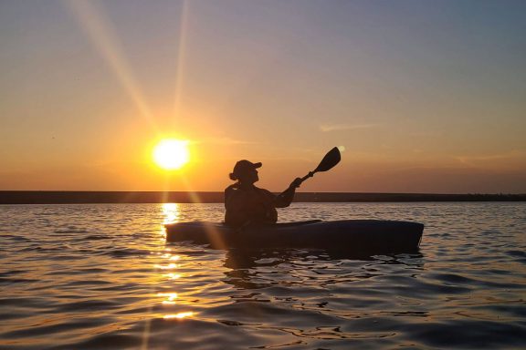 A woman kayaks at sunset on a lake.