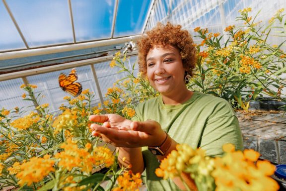 a woman stands among yellow-orange flowers and releases a monarch