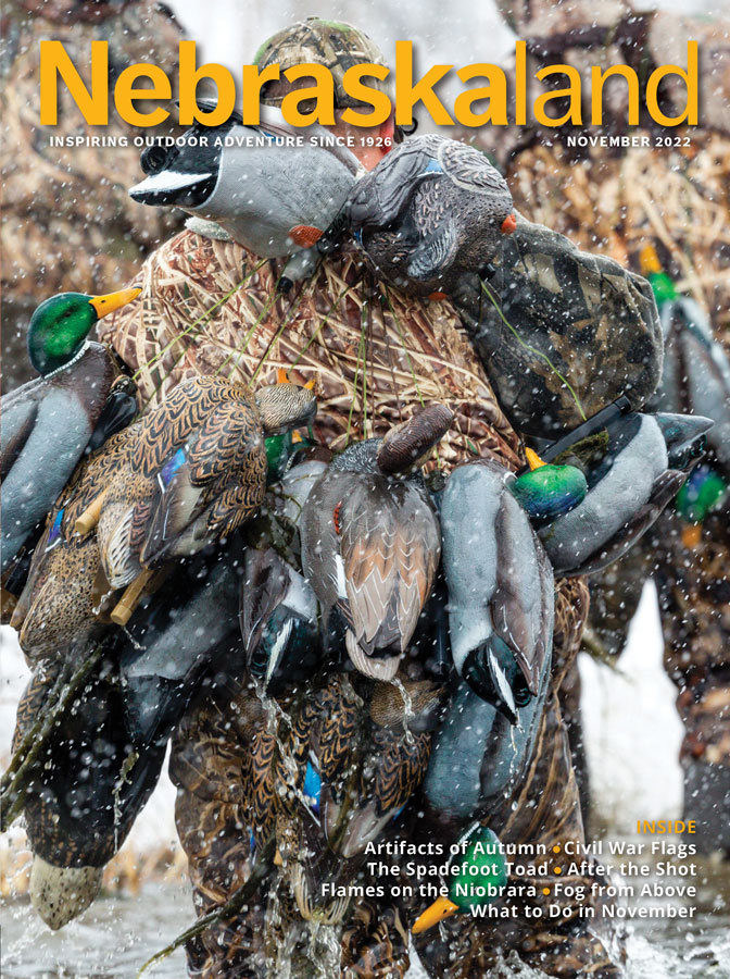 November 2022 Nebraskaland cover featuring a duck hunter carrying decoys in water.