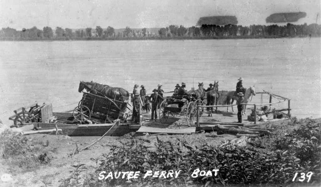 a rickety plank ferry with paddlewheels is loaded with wagons and carts