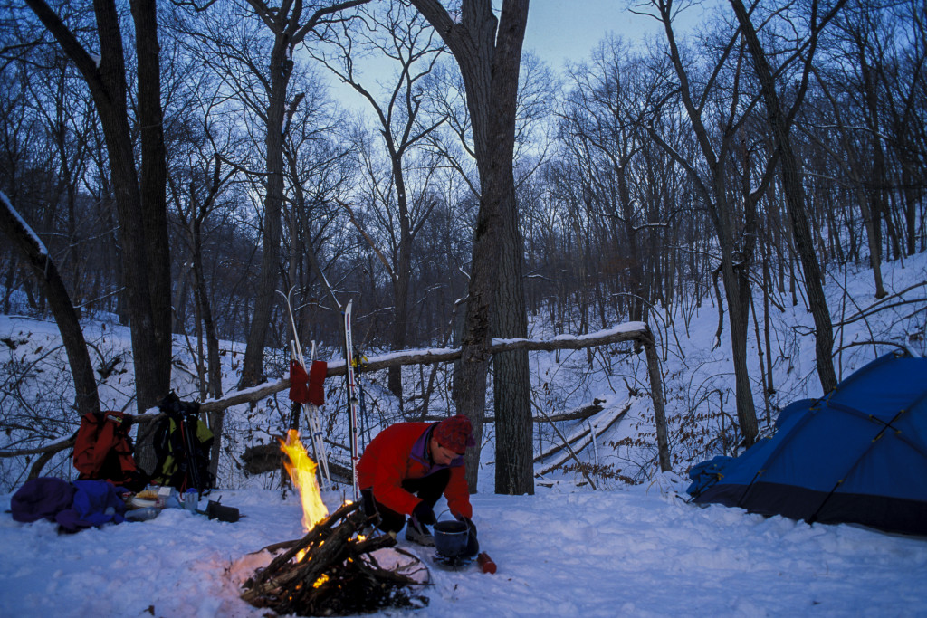 a man crouches over a pot in the snow