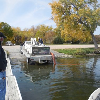 a man watches on as a truck loaded with fish back into a lake to stock trout