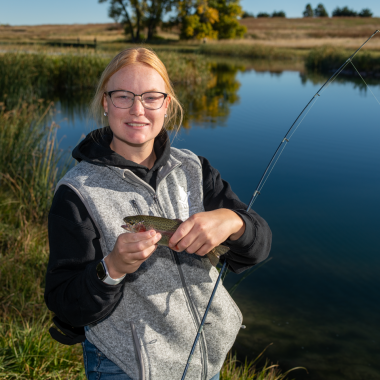 a blond woman holds a small trout