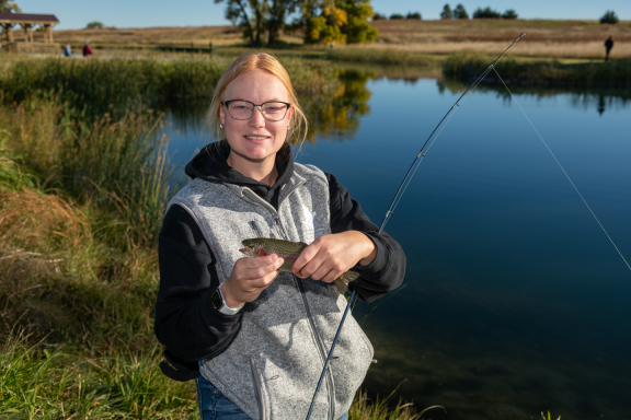 a blond woman holds a small trout