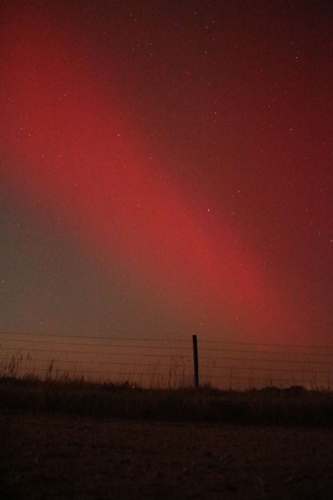 Reddish color northern lights display over a barbed wire fence.