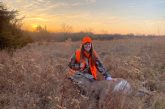 A woman poses at sunset in a field with a harvested deer.