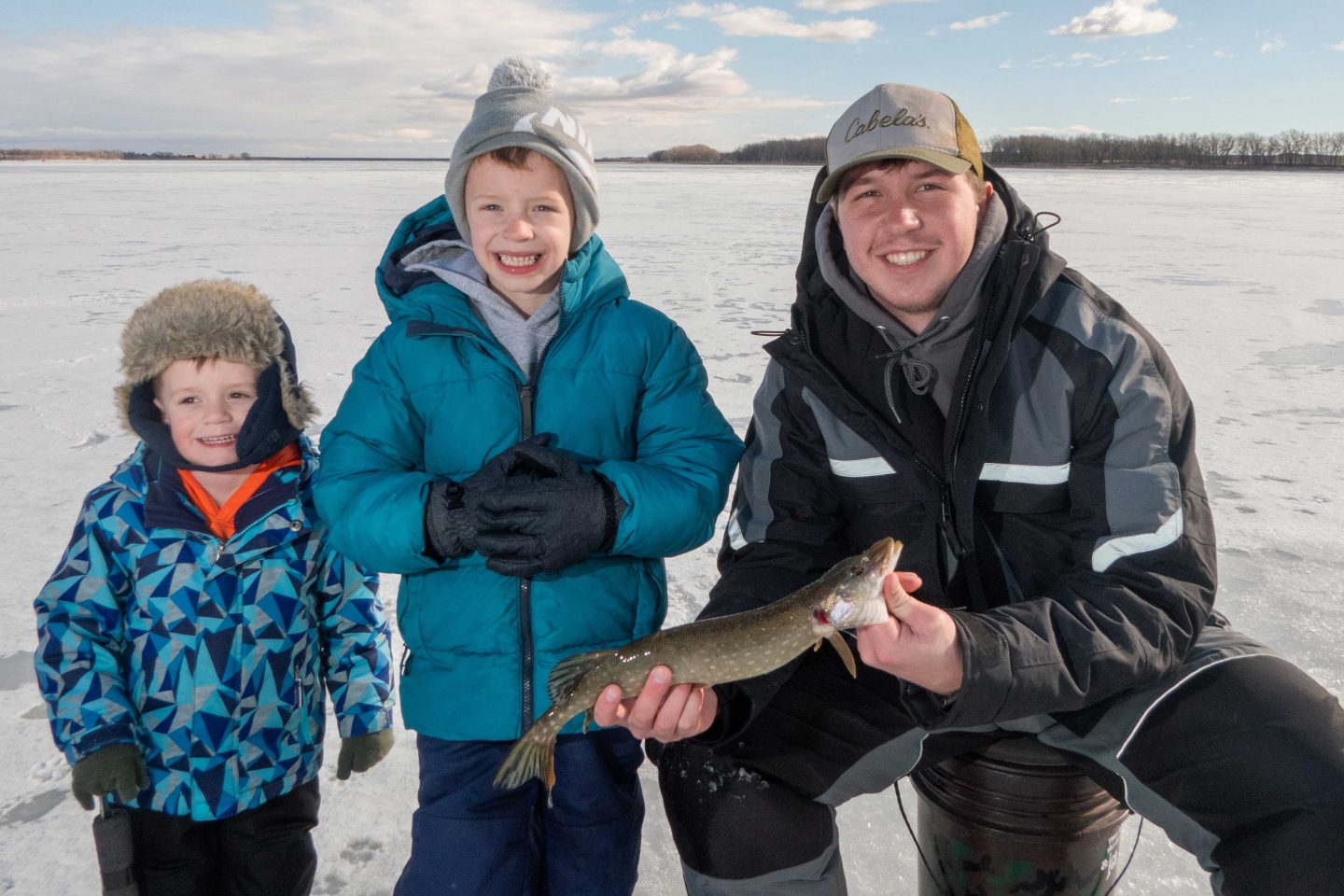 An older boy ice fishing with two younger boys.