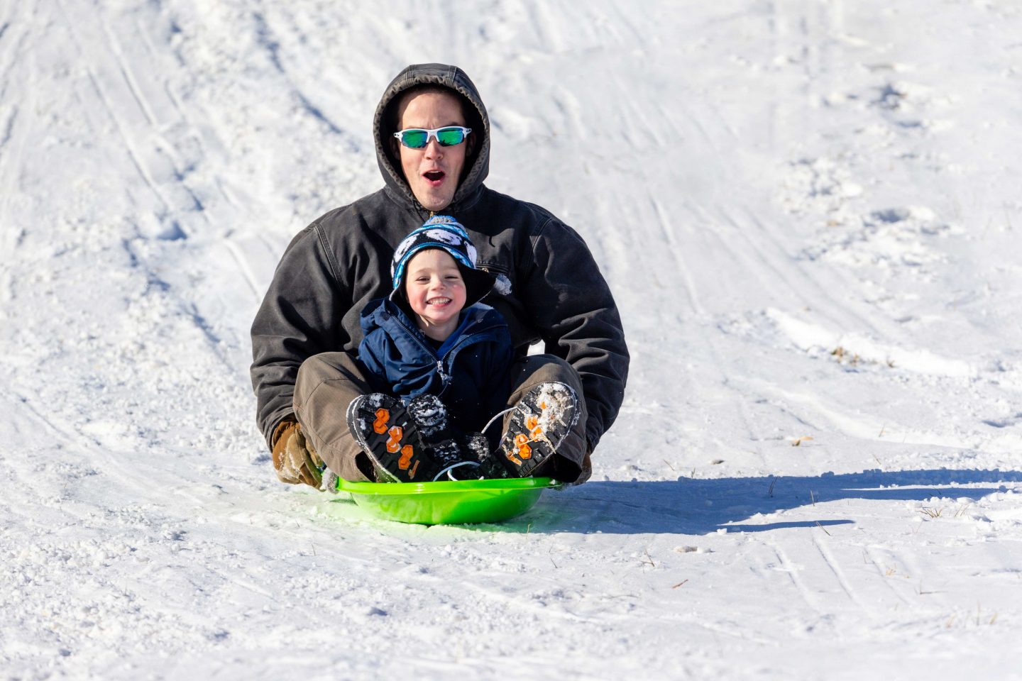 Dad and son sledding down a snow-covered hill.