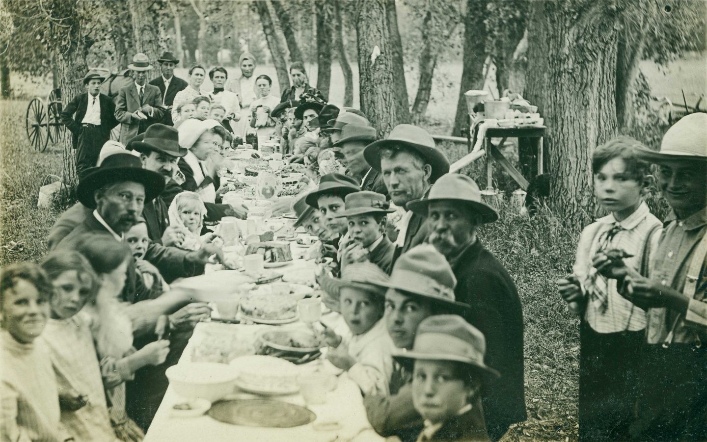 Black and white photo of people sitting down for a meal at a long table outdoors.