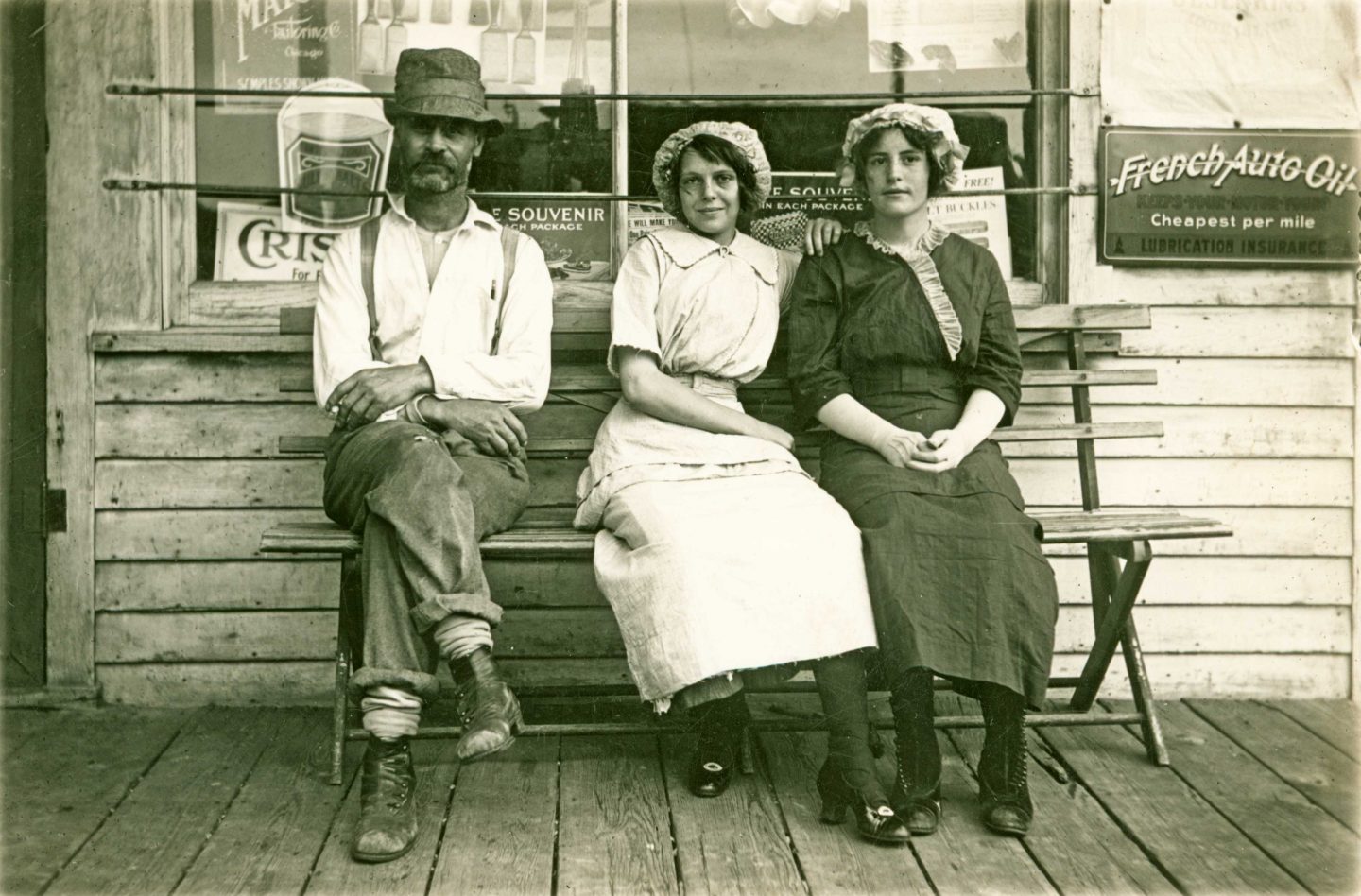 Black and white photo of a man and two women sitting outside general store.