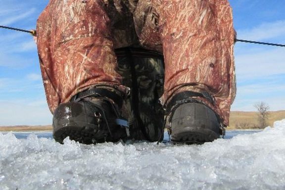 Boots with creepers next to an ice hole.