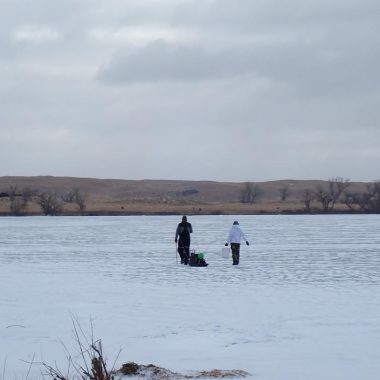 Two anglers walking onto a frozen lake.