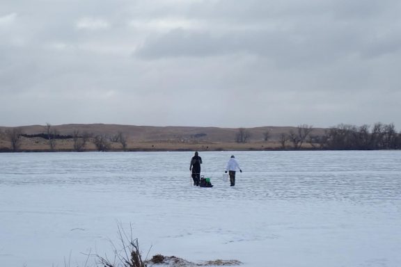 Two anglers walking onto a frozen lake.