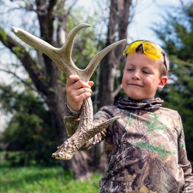 A boy holds up a deer shed he found outdoors.