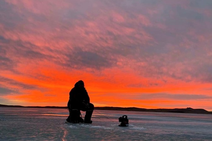 Sunset silhouetting an ice angler.