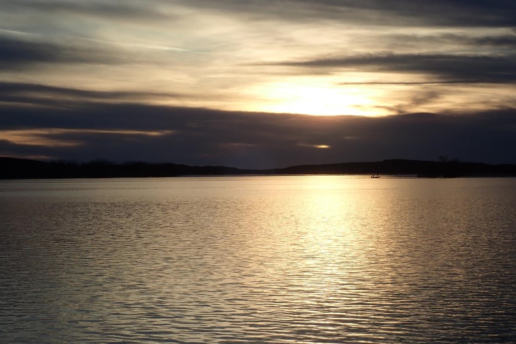 Sunset over water, boat on lake.  Photo by Daryl Bauer.