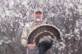 Hunter holding a tom turkey, posed in front of wild plums in bloom.