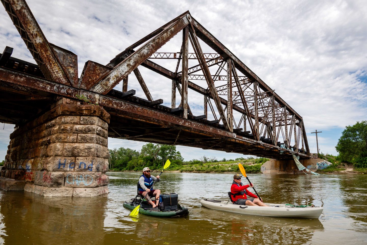 Two men kayaking underneath a bridge.