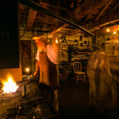 This photo, taken with a slow shutter speed during a Candlelight Tour, shows blacksmiths Doug Appel at the forge, Slader’s ghost-like form hammering at the anvil to the right and Lauren Joyce sitting at the work bench in the back.