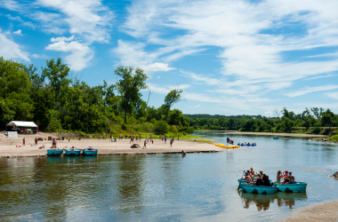 people in blue round vessels float past a sandy beach under bright blue skies