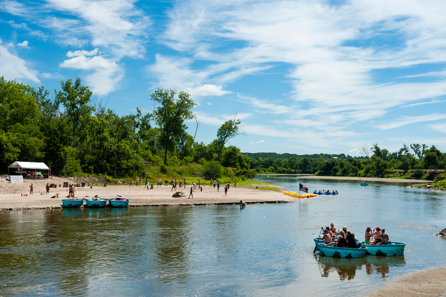 people in blue round vessels float past a sandy beach under bright blue skies