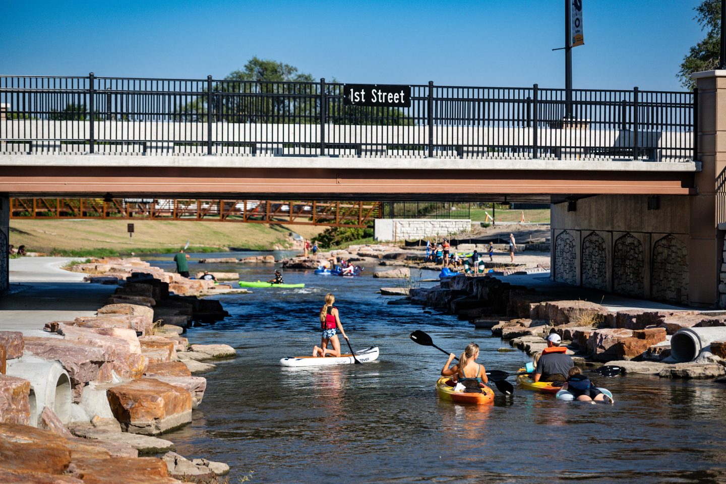A family rides a stand-up paddleboard, kayaks and a tube down the North Fork beneath the 1st Street bridge.