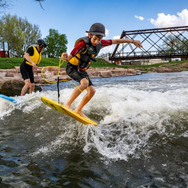 ﻿Jacob Stuthman of Norfolk does a trick on a boogie board as his dad, Tony, rides a surfboard on the surf wave on the North Fork Whitewater Trail in Norfolk.
