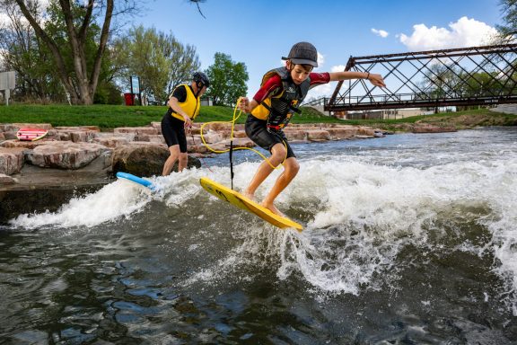 ﻿Jacob Stuthman of Norfolk does a trick on a boogie board as his dad, Tony, rides a surfboard on the surf wave on the North Fork Whitewater Trail in Norfolk.
