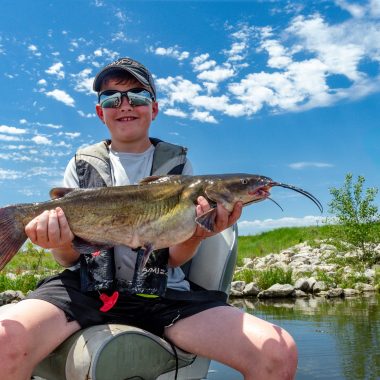 A boy holding a catfish he caught.
