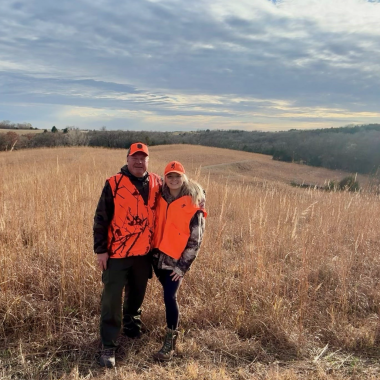 A father and daughter pose in a field during fall hunting season in Nebraska.