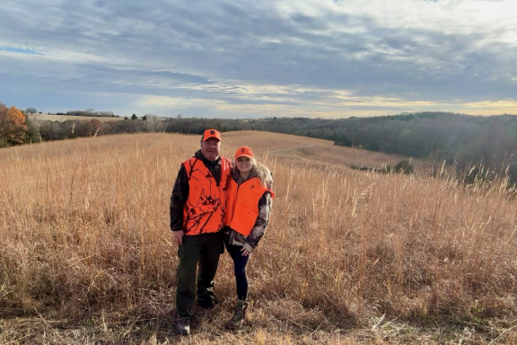 A father and daughter pose in a field during fall hunting season in Nebraska.