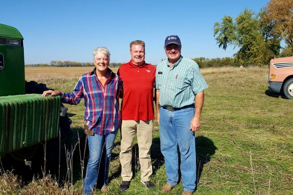 Three people stand by farm equipment in rural Nebraska.