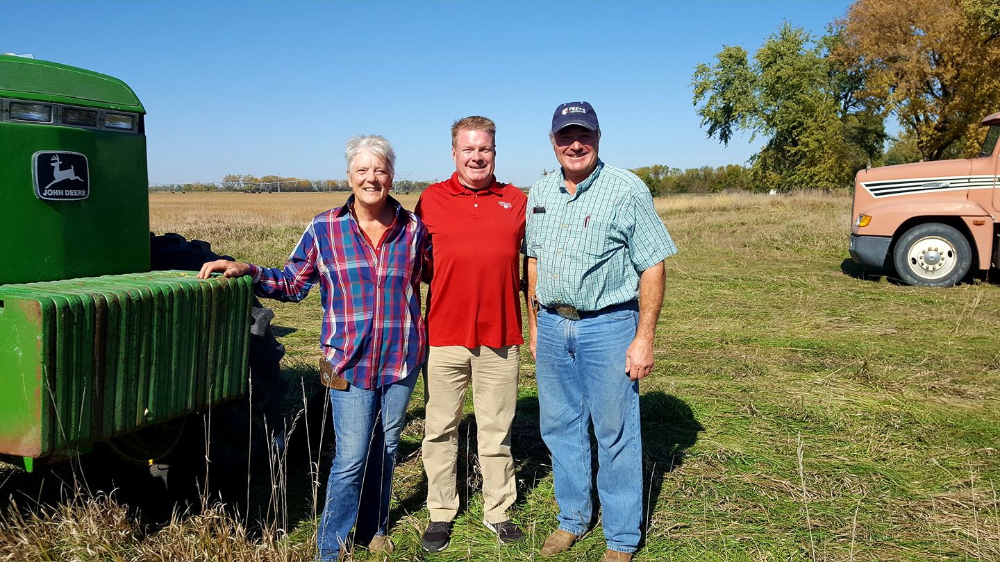 Three people stand by farm equipment in rural Nebraska.