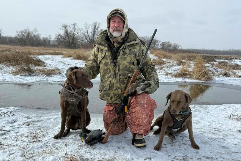 Hunter posing with dogs, decoy, shotgun and drake mallard. Photo by Emily Brown.