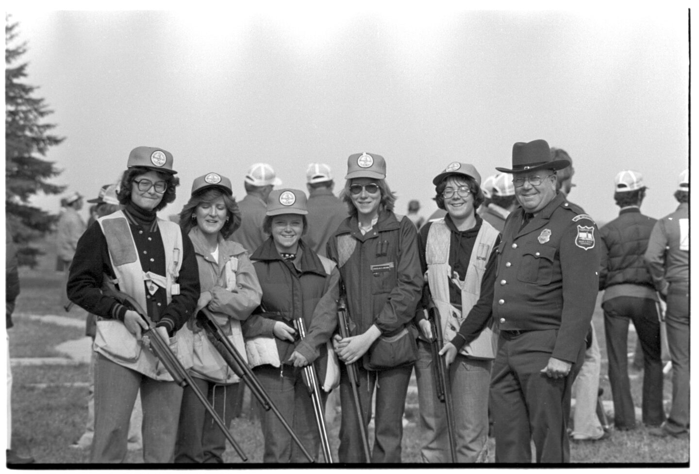 Cornhusker Invitational State Trap Shoot, Doniphan. High school and college. Group of female participants pose with a conservation officer. Photographer unattributed [Rocky Hoffmann or Rex Amack], April 1977. Copyright Nebraskaland Magazine/Nebraska Game and Parks Commission.