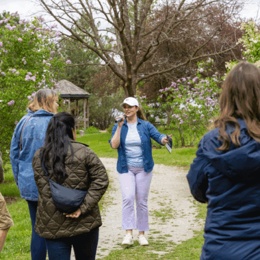 A woman holding a microphone stands on a lilac path