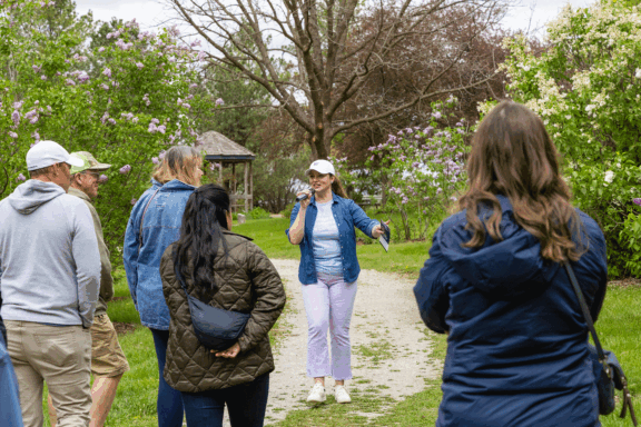 A woman holding a microphone stands on a lilac path