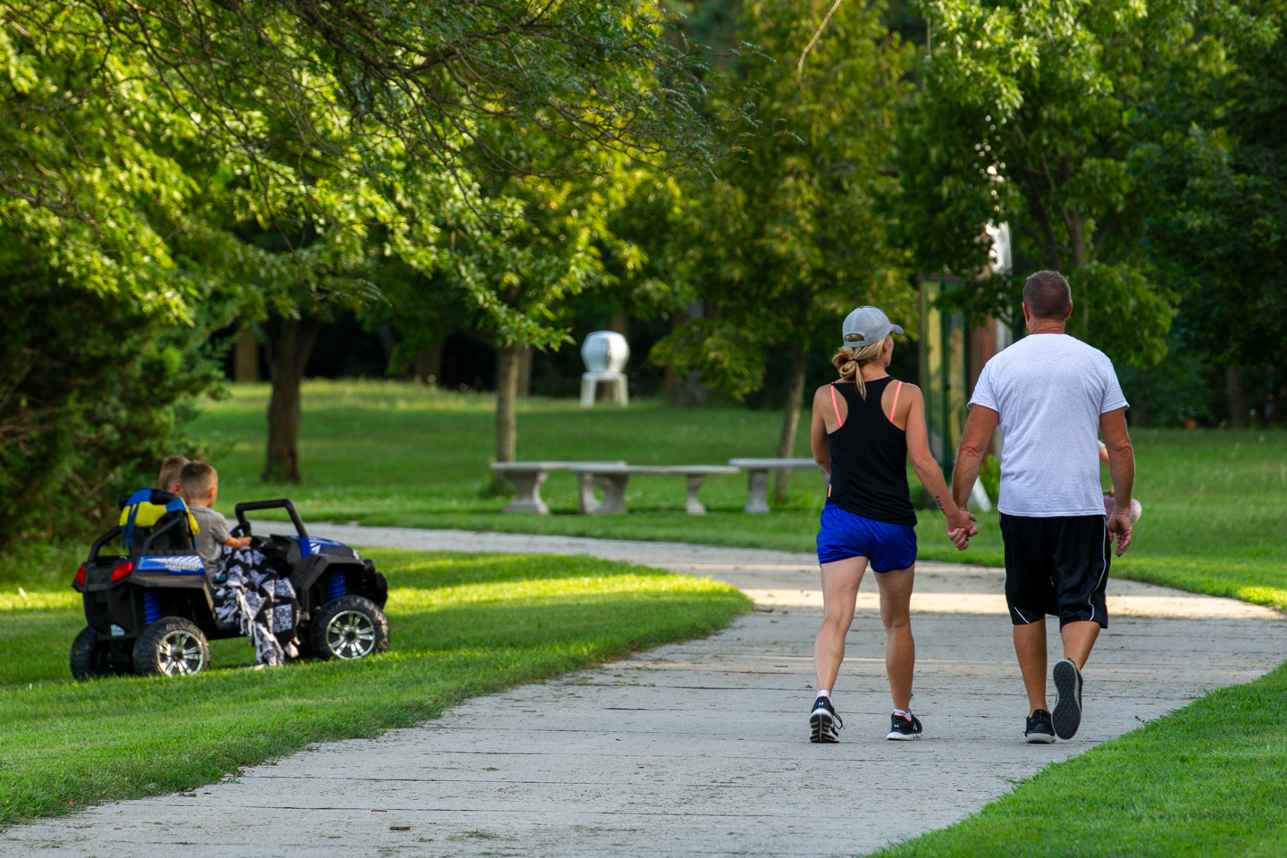 A man and woman holding hands and walking on a paved trail at a park.