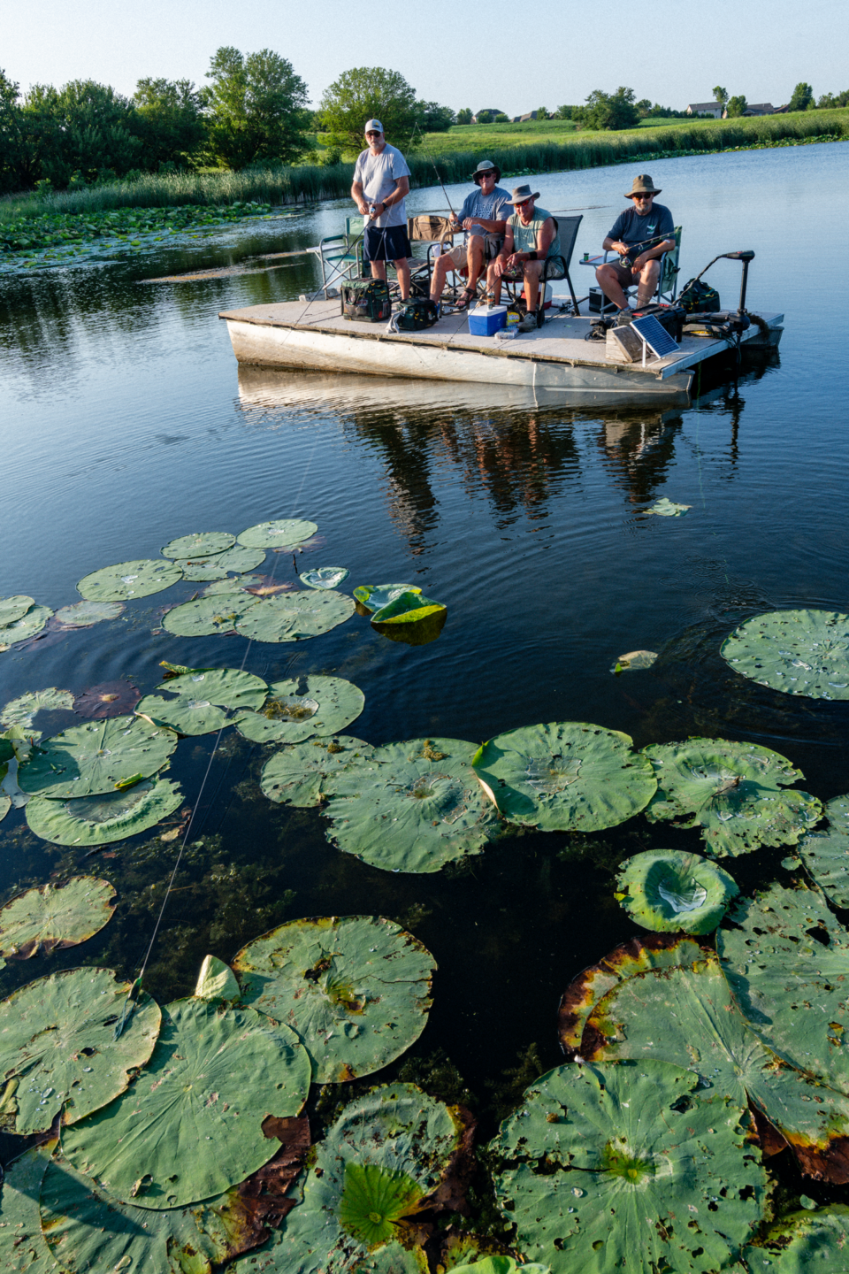 A group of men fishing from a boat on a pond.