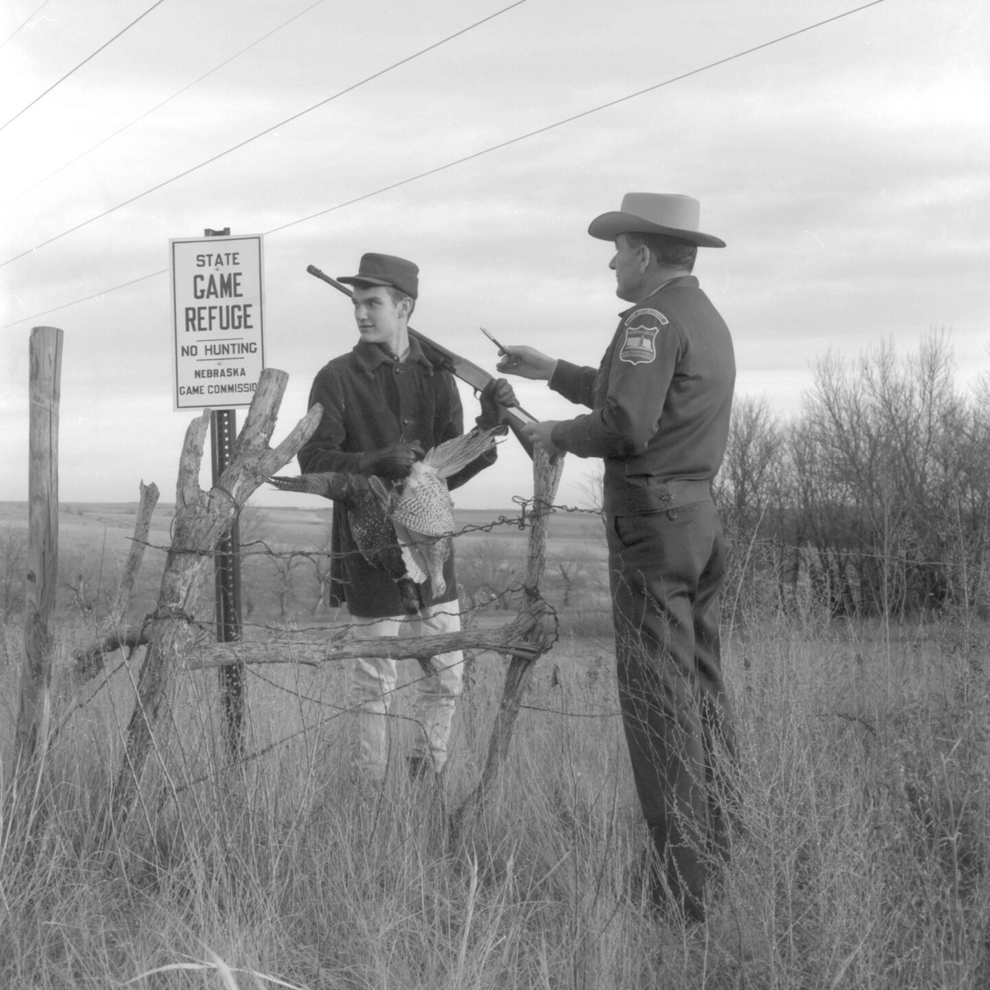 Conservation officer Carl Gettmann points out a “no hunting” sign on a game refuge to a teenage boy carrying a firearm and bagged pheasants.