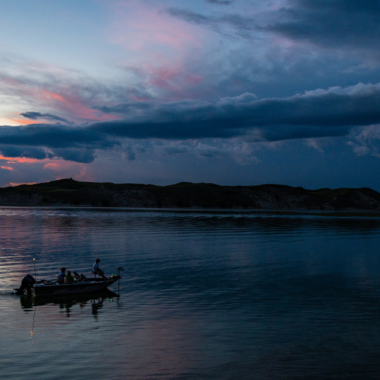 Anglers fish from a boat in the Nebraska Sandhills during summer as the sun sets.